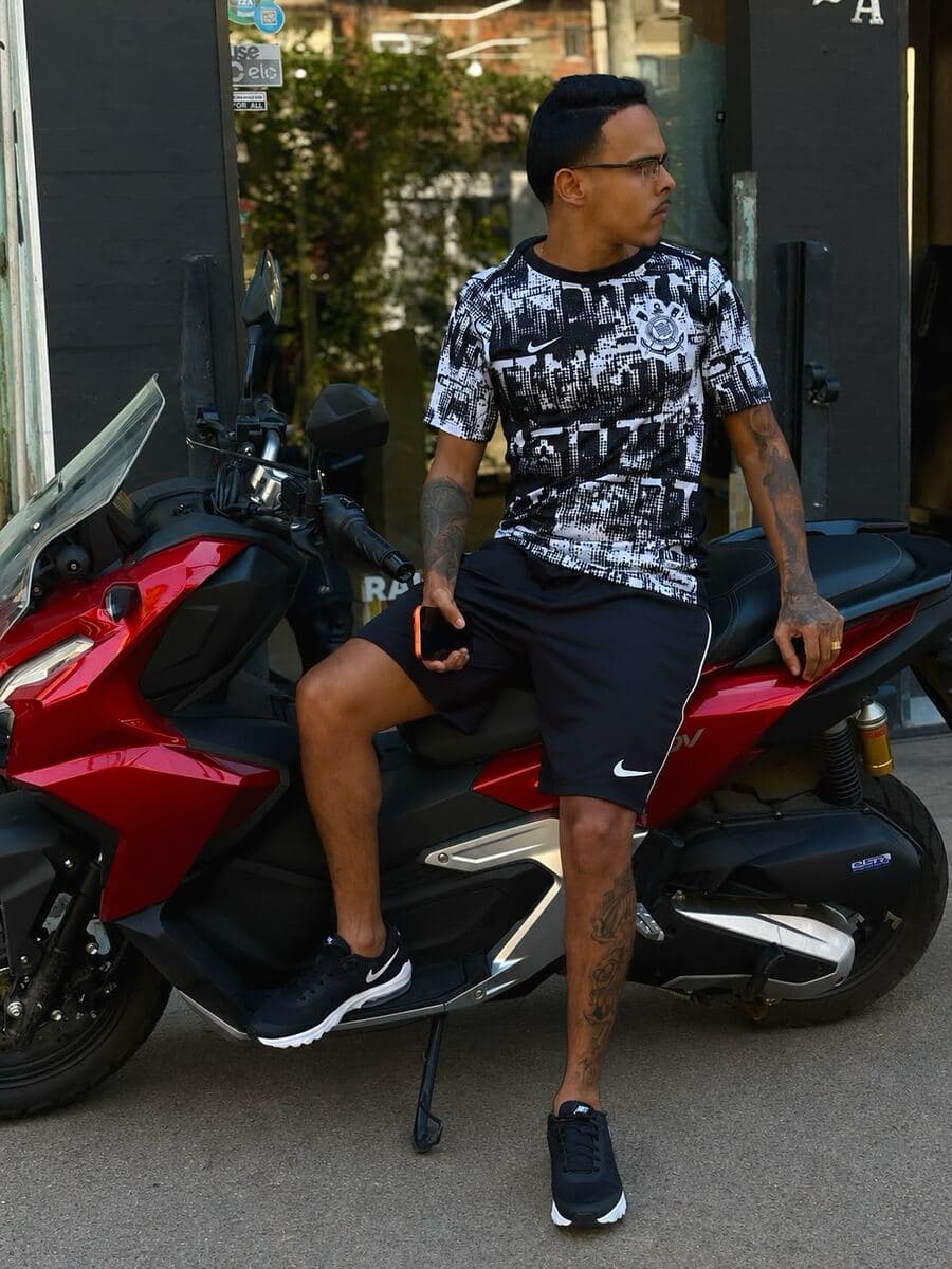 Cria de camisa estampada e short preto, na moto na frente da loja