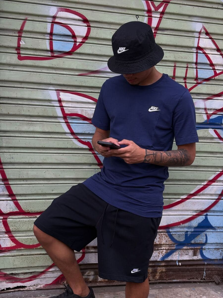 Cria de camiseta azul-marinho e boné bucket Nike, de frente para o grafite